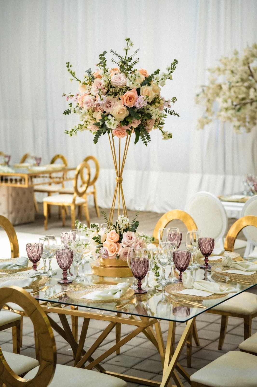 Mesa de vidrio sobre base dorada con cristales colgantes y centro floral alto en la boda de Daya y Marco