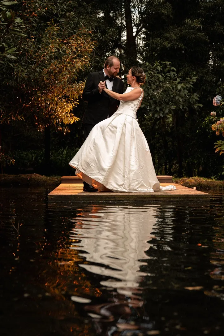 Primer baile de una pareja sobre el muelle, reflejados en el agua, en una boda real en Puembo, Quito