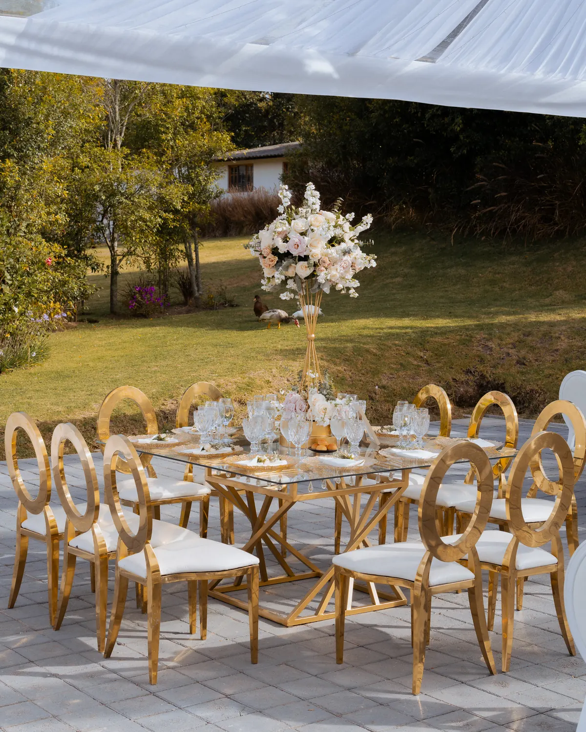 Mesa de vidrio sobre base geométrica dorada con sillas Infinity en la boda de Sol y Gus, Villa Lagos